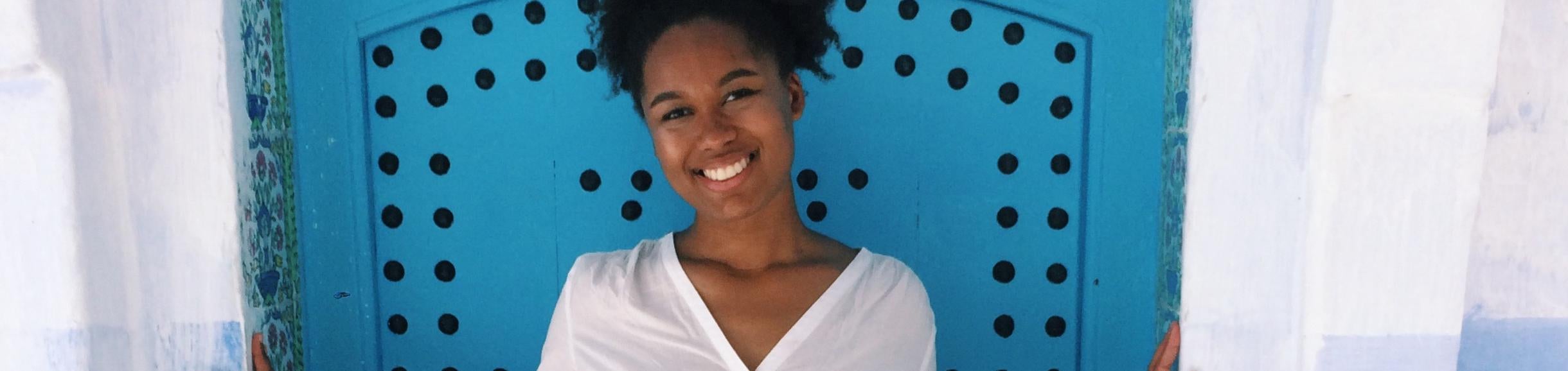 Female UCR student posing by blue door